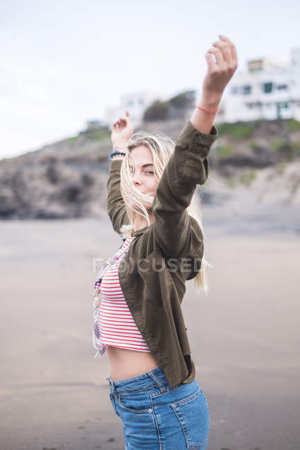 Portrait de jeune femme blonde debout sur la plage avec les bras levés — Photo de stock