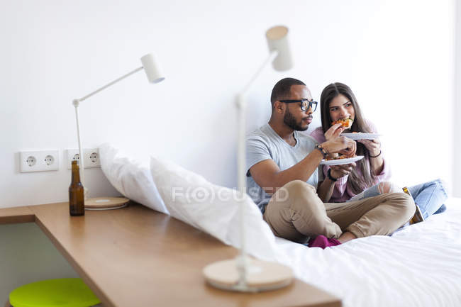 Ritratto di una giovane coppia che mangia sul letto — Foto stock