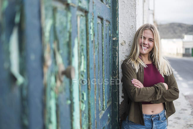 Portrait de jeune femme blonde avec les bras croisés debout à côté de la vieille porte en bois — Photo de stock