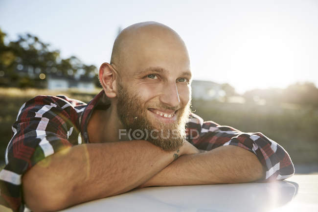 Porträt eines jungen Mannes mit Glatze und Bart, der auf dem Autodach lehnt — Stockfoto