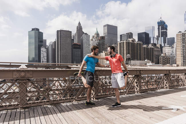 USA, New York, ponte di Brooklyn, due giovani in allenamento di fitness, vista sul paesaggio urbano sullo sfondo — Foto stock
