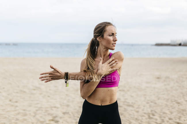 Jeune femme qui s'étire et se réchauffe pour s'entraîner à la plage — Photo de stock