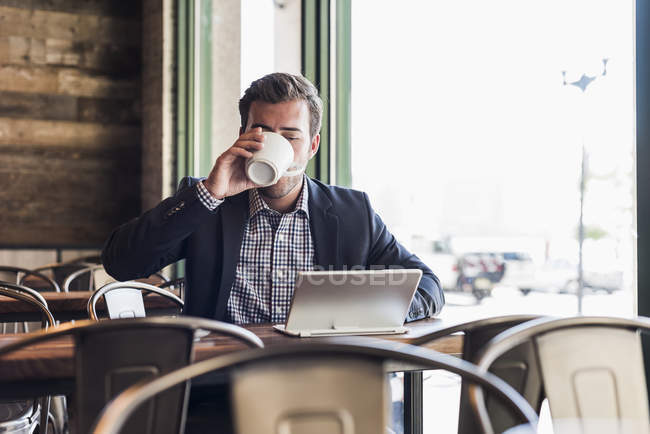 Geschäftsmann trinkt Kaffee und benutzt Tabletten in einem Café — Stockfoto