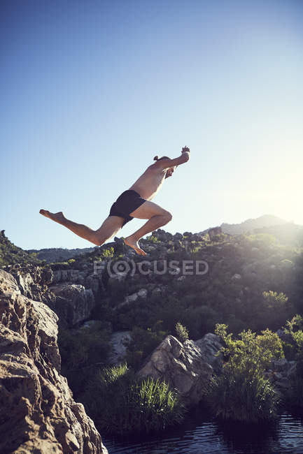 Hombre saltando de la roca al agua en la naturaleza - foto de stock