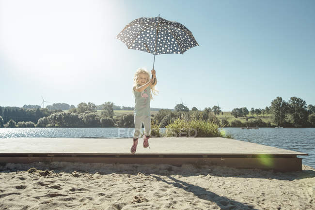 Ragazza che tiene un ombrello e salta giù da un molo il giorno asunny — Foto stock