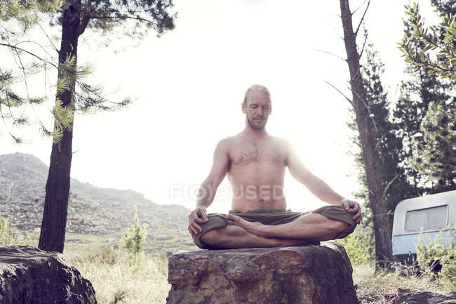Shirtless man practicing yoga on boulder in countryside — Stock Photo