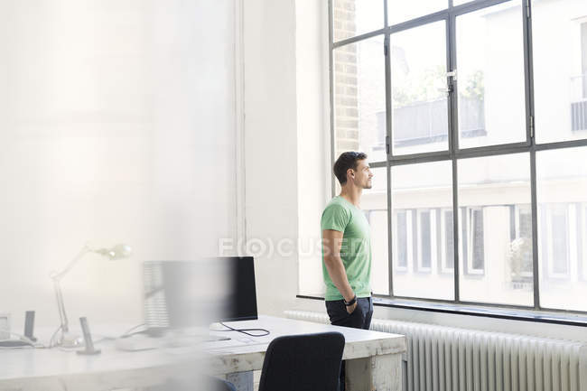Giovane uomo d'affari pensieroso che guarda fuori dalla finestra in ufficio — Foto stock