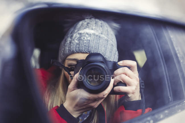 Espelho de asa com imagem de espelho de mulher tirando foto de si mesma, close-up — Fotografia de Stock