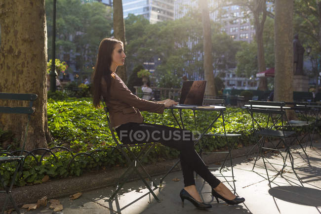 Giovane donna d'affari che lavora al parco cittadino seduta con laptop a tavola sotto il sole — Foto stock