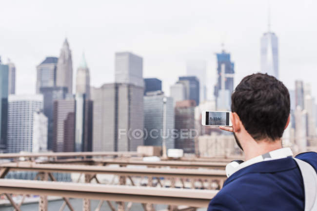 USA, New York, ponte di Brooklyn, Vista posteriore dell'uomo che scatta foto del paesaggio urbano con smartphone — Foto stock