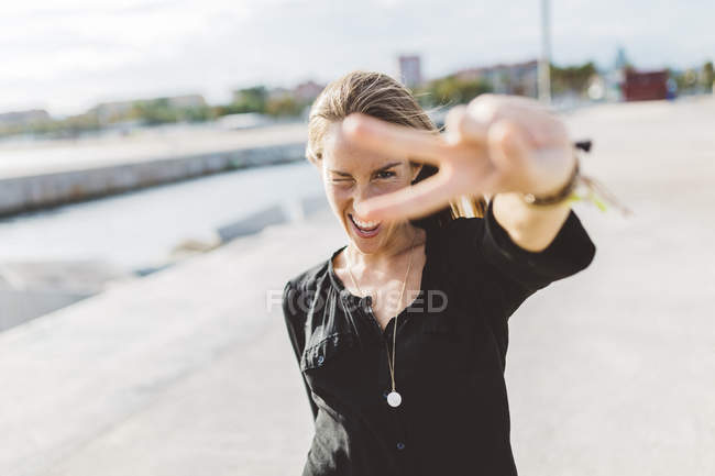 Joyeux jeune femme montrant signe de victoire à l'extérieur — Photo de stock