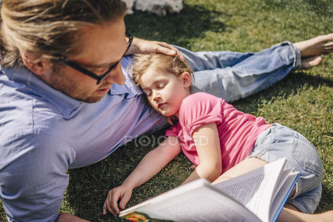 Батько читання книги, щоб спати дочка в саду — стокове фото