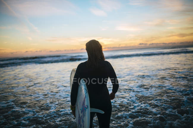 Spagna, Andalusia, Cadice, Conil de la Frontera, Surfista donna con tavola da surf che entra in mare al crepuscolo, vista da dietro
. — Foto stock