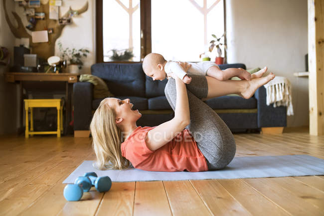 Bonne mère soulevant bébé à la maison tout en étant couché sur le tapis — Photo de stock