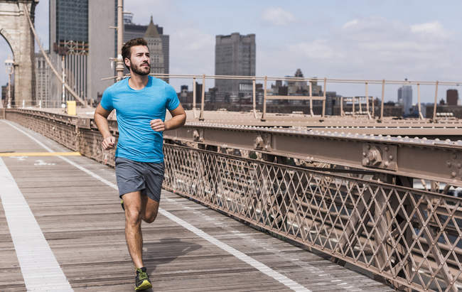 USA, New York, Brooklyn bridge, Young man jogging looking aside — Stock Photo