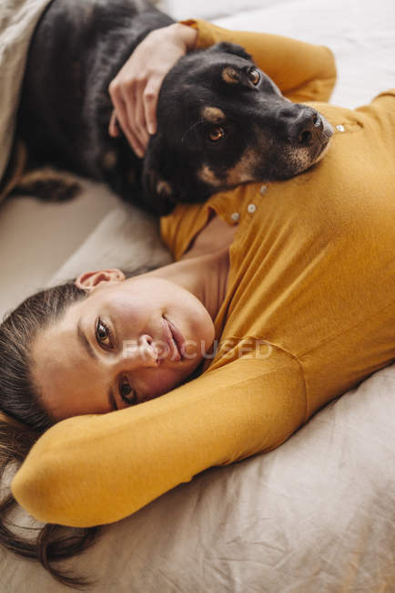 Femme détendue couchée au lit avec chien — Photo de stock