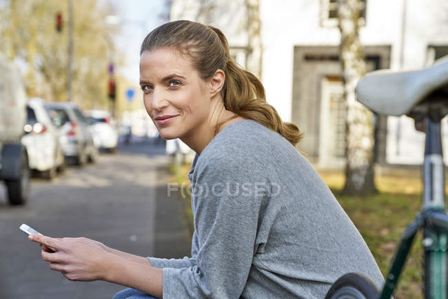 Portrait d'une femme blonde souriante assise avec un téléphone portable en ville — Photo de stock