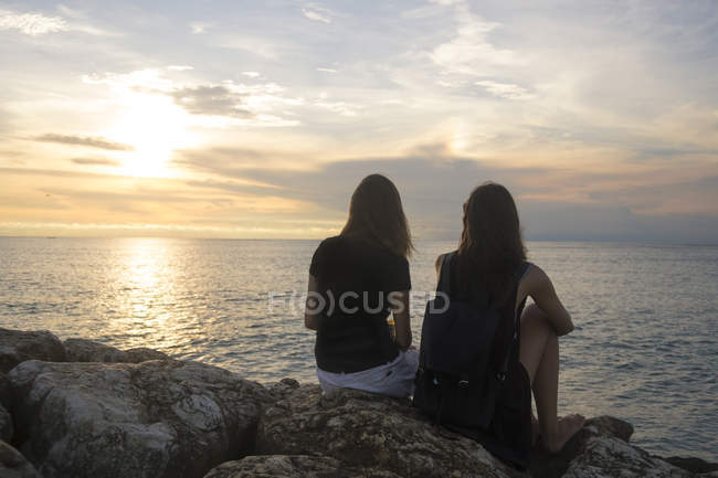 Indonesien, Bali, zwei Frauen, die den Sonnenuntergang über dem Ozean beobachten — Stockfoto