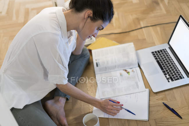 Young woman sitting on the floor and looking at notepad — Stock Photo