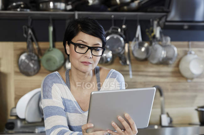 Femme dans la cuisine en utilisant une tablette numérique — Photo de stock