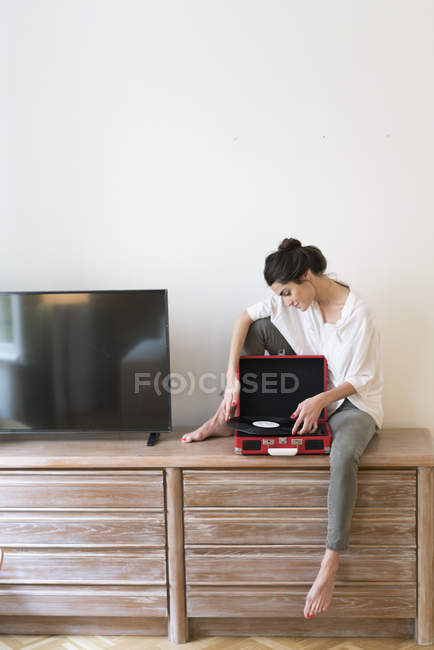 Woman sitting on chest of drawers with record and record player — Stock Photo