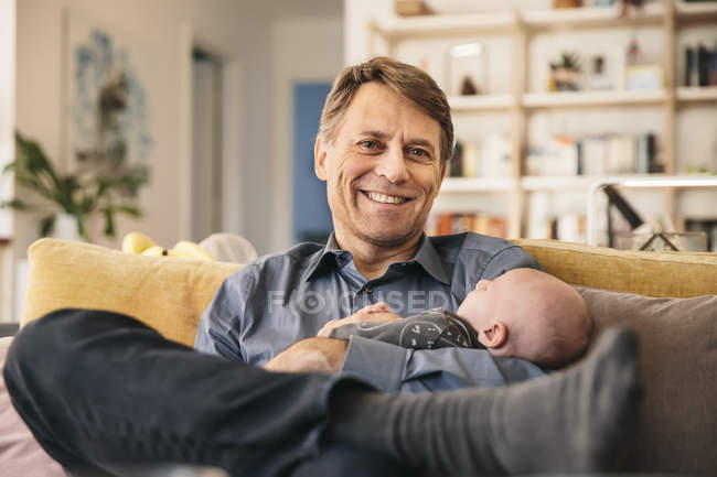 Father and newborn baby sitting on couch at home — Stock Photo