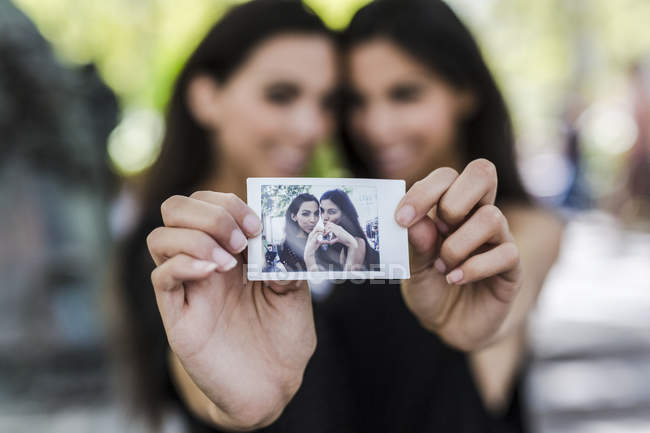 Twin sisters holding instant photo — Stock Photo