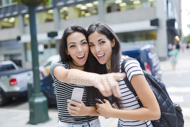 Twin sisters standing with cell phones in city — Stock Photo