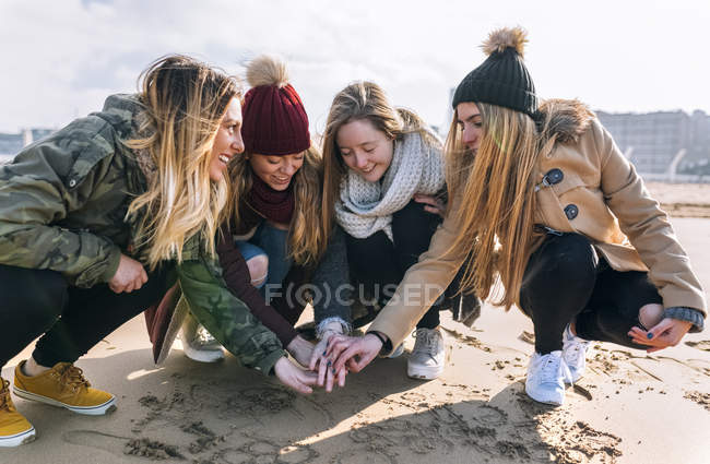Quatro amigos unindo as mãos na praia arenosa — Fotografia de Stock