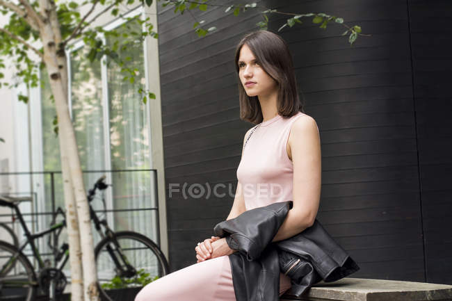 Retrato de jovem sentada no banco e segurando jaqueta preta — Fotografia de Stock