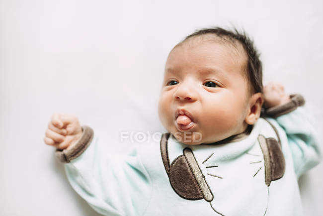 Bebé recién nacido sacando la lengua usando camiseta con auriculares - foto de stock