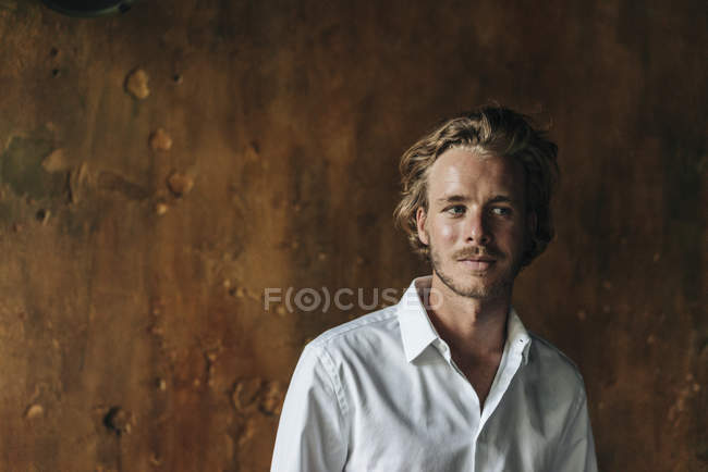 Ritratto di uomo biondo che indossa una camicia bianca in piedi davanti all'intonaco marrone — Foto stock