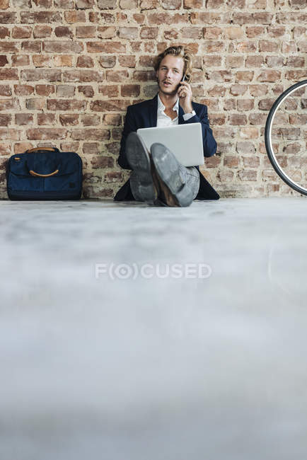 Geschäftsmann sitzt auf dem Boden und benutzt Laptop mit Handy — Stockfoto