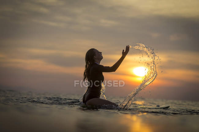 Surferin planscht bei Sonnenuntergang im Ozean — Stockfoto
