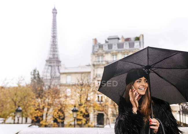 Parigi, Francia, giovane donna che usa lo smartphone sotto la pioggia con la Torre Eiffel sullo sfondo
. — Foto stock