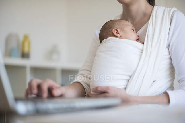 Geschnittenes Bild einer freiberuflichen Mutter mit Säugling im Tragetuch bei der Arbeit im Home Office — Stockfoto