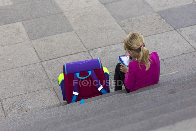 Back view of little girl with school bag sitting on stairs doing homework — Stock Photo