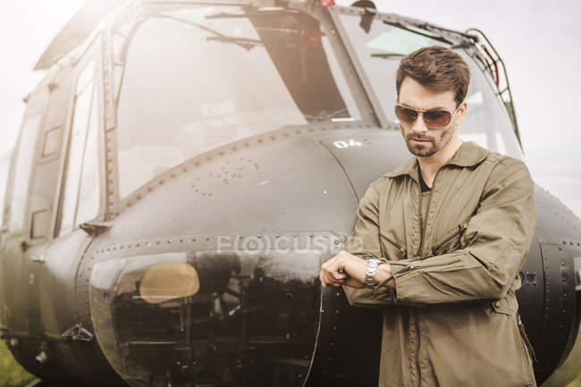Man in overall standing next to a helicopter and checking the time — Stock Photo