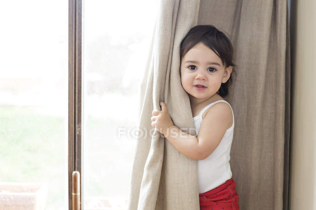 Portrait Of A Toddler Girl Playing Peek A Boo Behind The Curtains