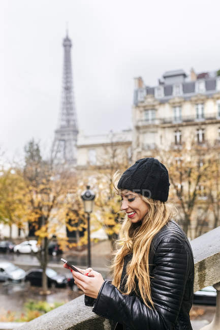 Paris, France, jeune femme utilisant son smartphone avec la Tour Eiffel en arrière-plan . — Photo de stock