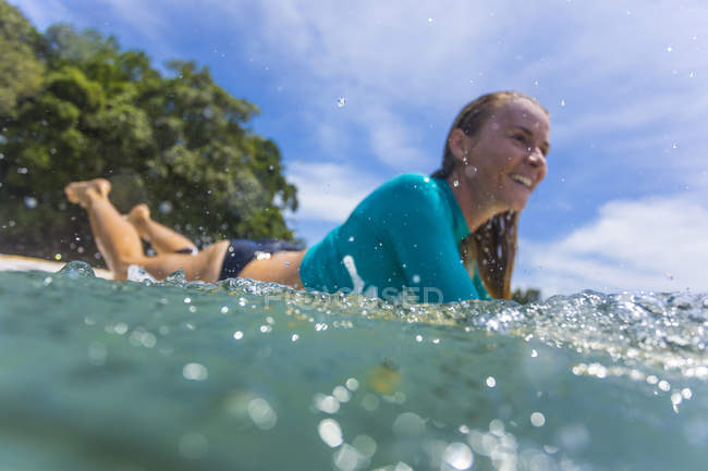 Indonesia, Java, mujer sonriente acostada en la tabla de surf en el mar - foto de stock