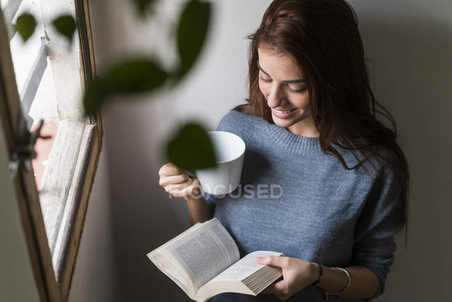 Attrayant jeune femme lecture livre et boire du café — Photo de stock