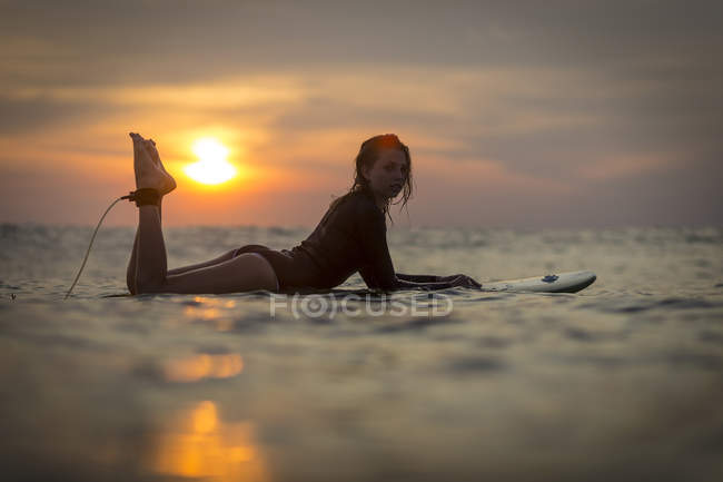 Surfeuse dans l'océan au coucher du soleil avec un ciel romantique — Photo de stock