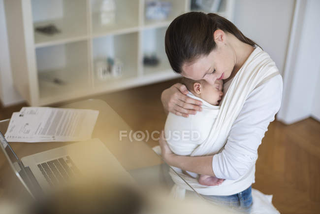 Vue élevée de la mère pigiste étreignant bébé en fronde au bureau à la maison — Photo de stock