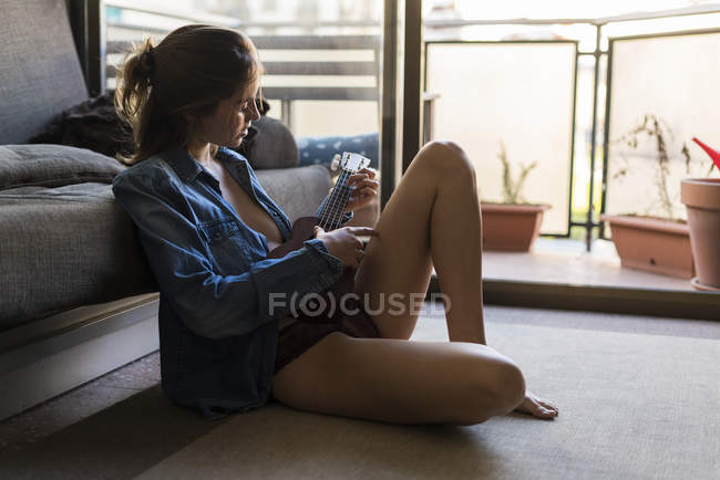 Jovem mulher jogando ukulele em casa — Fotografia de Stock