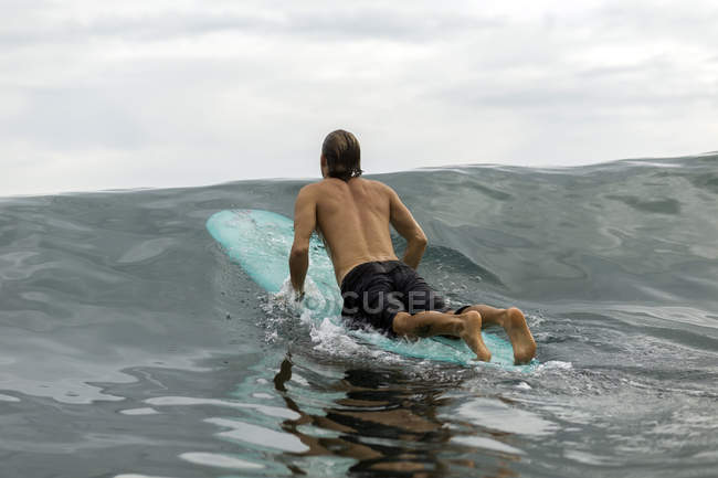 Indonésia, Java, homem deitado na prancha de surf no mar — Fotografia de Stock