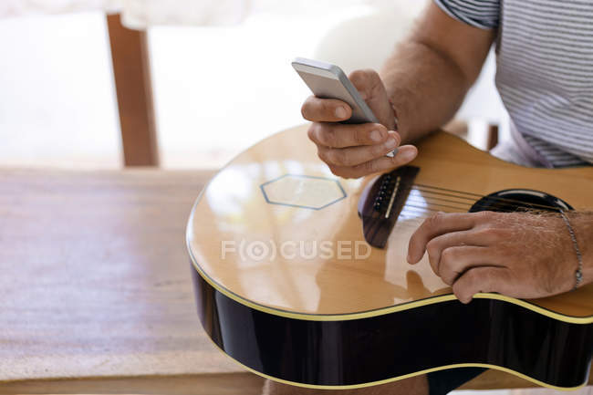 Primer plano del hombre sosteniendo la guitarra y el teléfono celular - foto de stock