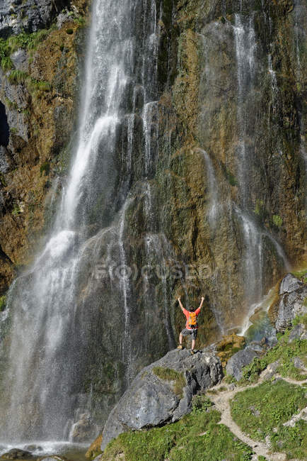 Austria, Tirol, Montañas Rofan, excursionista de pie en la cascada Dalfaz con los brazos levantados - foto de stock