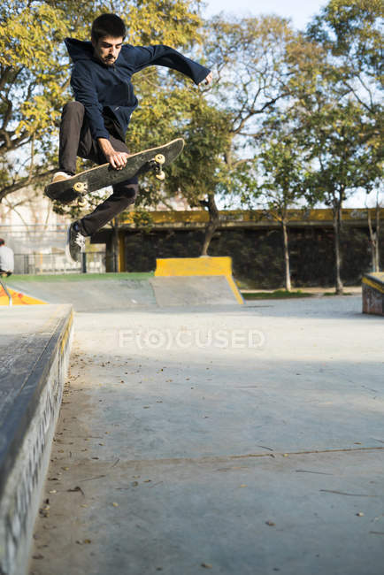 Skater boy engañando en skatebard saltando por la rampa en skate park - foto de stock
