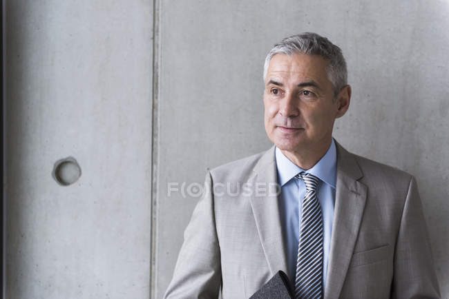 Hombre de negocios de pie frente a la pared gris - foto de stock